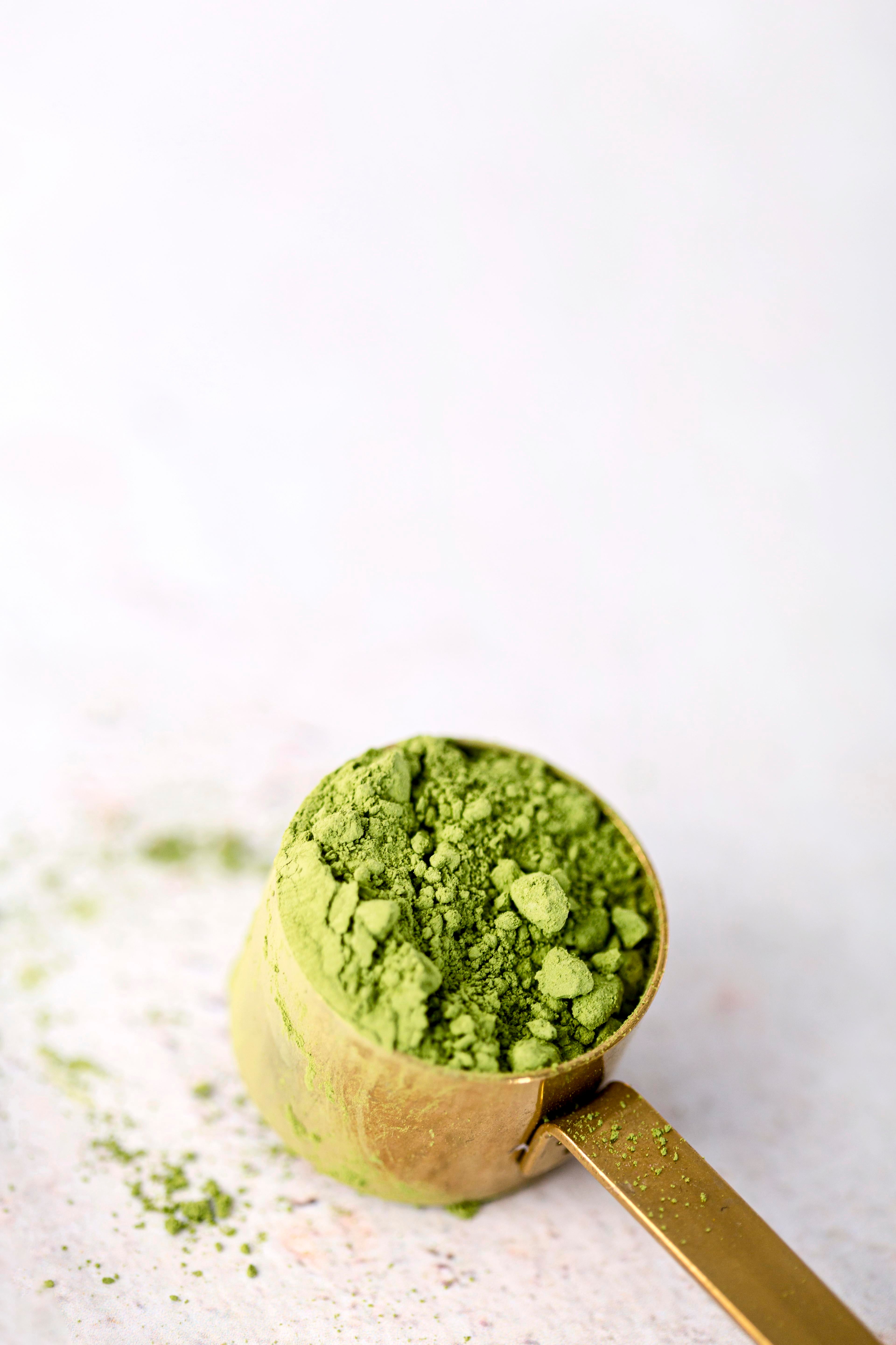 Gold measuring spoon filled with matcha green tea powder on a white background